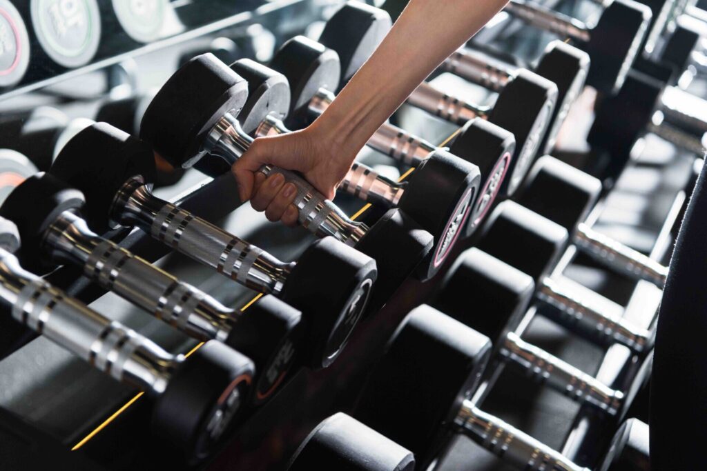 Close-up of a person's hand grabbing a chrome dumbbell handle from a gym rack filled with weights