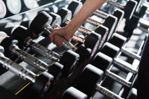 Close-up of a person's hand grabbing a chrome dumbbell handle from a gym rack filled with weights