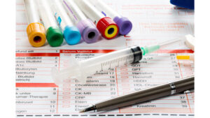 An empty plastic syringe lying across German medical lab forms next to colorful blood collection tubes