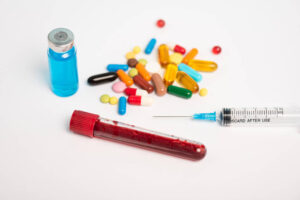 Syringe, vial of blood, and pills on a white surface.