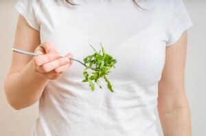 Young vegetaian woman is eating leaves of ruccola. Diet and heal