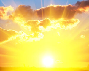 Bright yellow sun breaking through dramatic clouds, casting powerful sunbeams downward