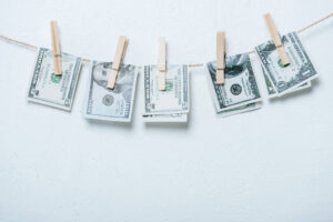 Several United States dollar bills hanging on a clothesline, attached with wooden clothespins against a white wall