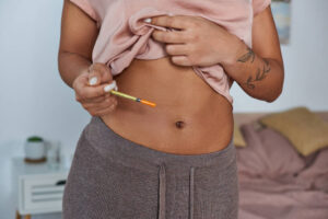 Close-up of a person holding a small syringe to administer an injection into their abdomen