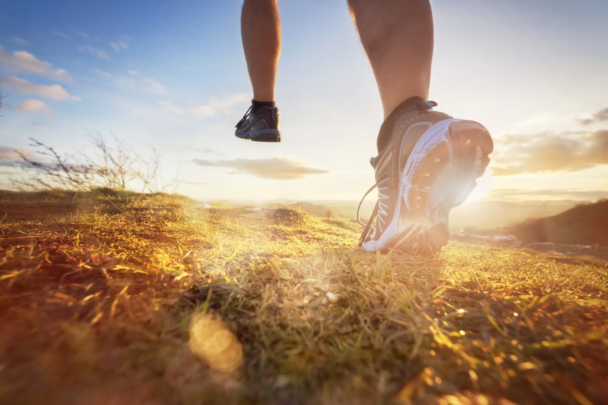 Close-up of a person's feet running on a grassy trail during a golden sunset