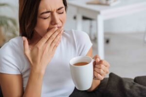 woman yawning while holding a cup of coffee