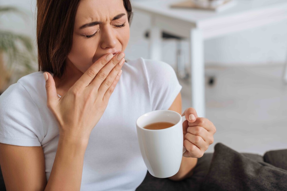 woman yawning while holding a cup of coffee