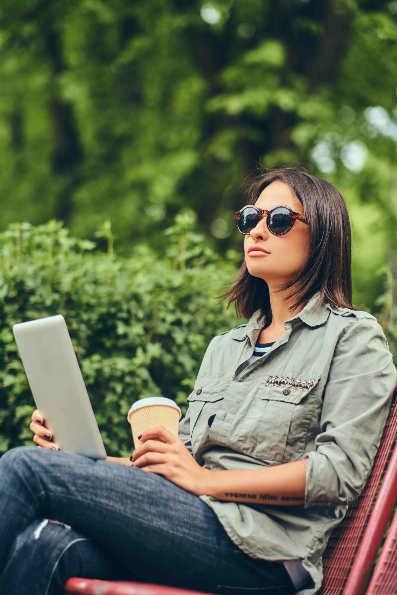 Woman working on a laptop outdoors while enjoying fresh air and a cup of coffee