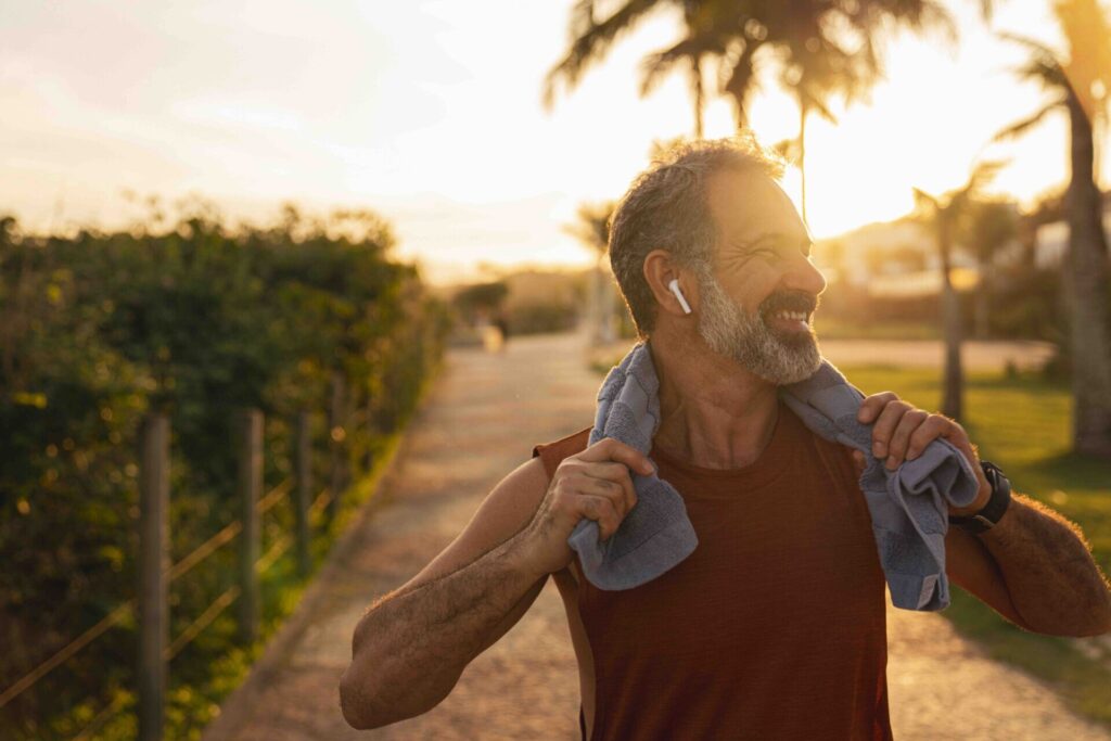 Smiling middle-aged man with a towel over his shoulders standing outdoors after exercise at sunset