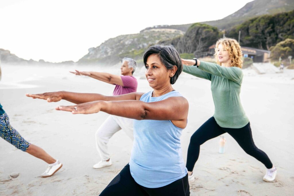 A group of middle-aged sporty women exercising along the beach in athletic wear. Their posture and synchronized strides reflect energy, fitness, and an active lifestyle showing the benefits of the Flow Wellness health and wellness programs.