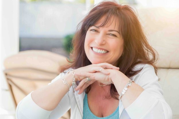 Smiling middle-aged woman with dark hair sitting indoors with her hands resting under her chin